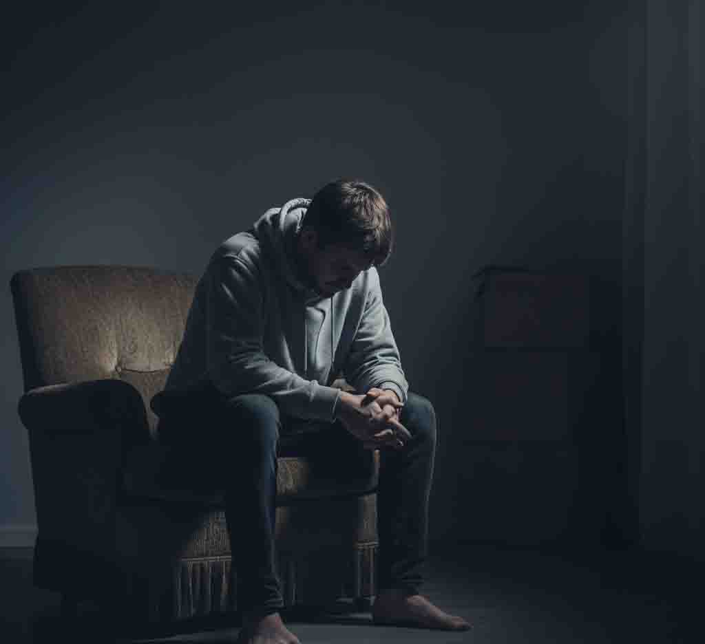 A person sitting alone, looking downcast, with a muted and dark background to symbolize feelings of isolation and sadness.